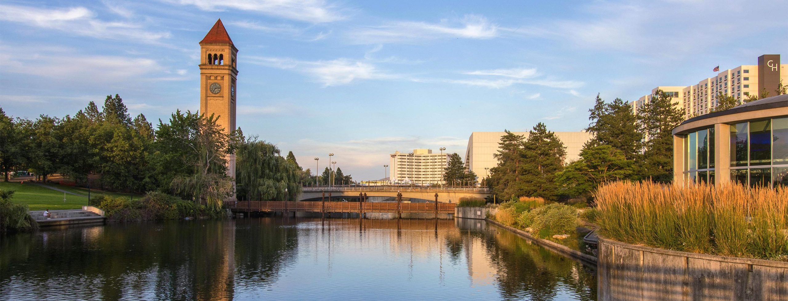 A serene lake view with a clock tower and modern buildings.